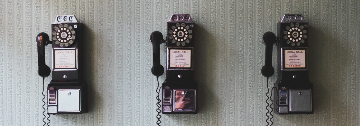 three rotary pay phones on a wall